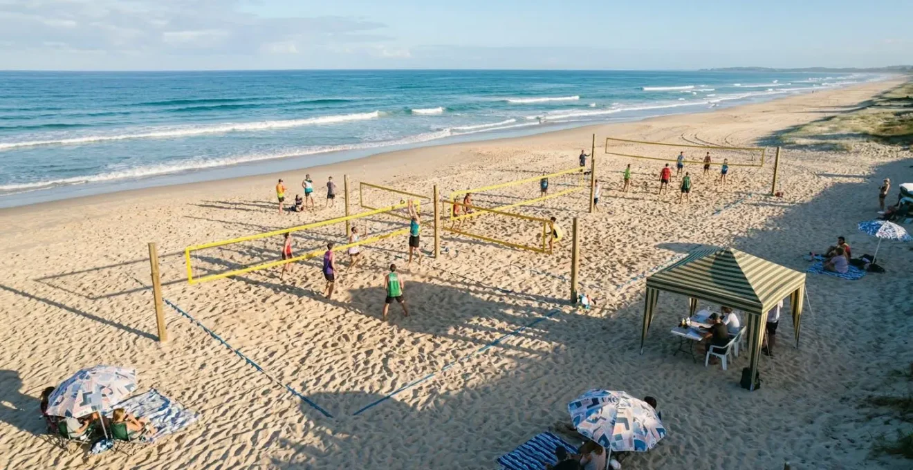 Vue aérienne d'un tournoi de beach-volley amateur sur une plage publique avec plusieurs terrains installés