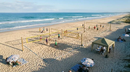 Vue aérienne d'un tournoi de beach-volley amateur sur une plage publique avec plusieurs terrains installés
