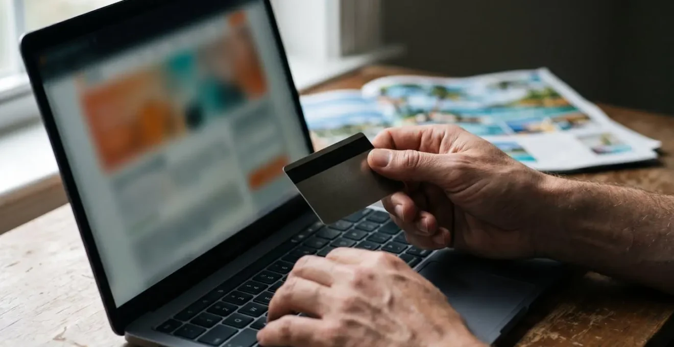 Mains tenant une carte bancaire devant un écran d'ordinateur flou montrant une transaction